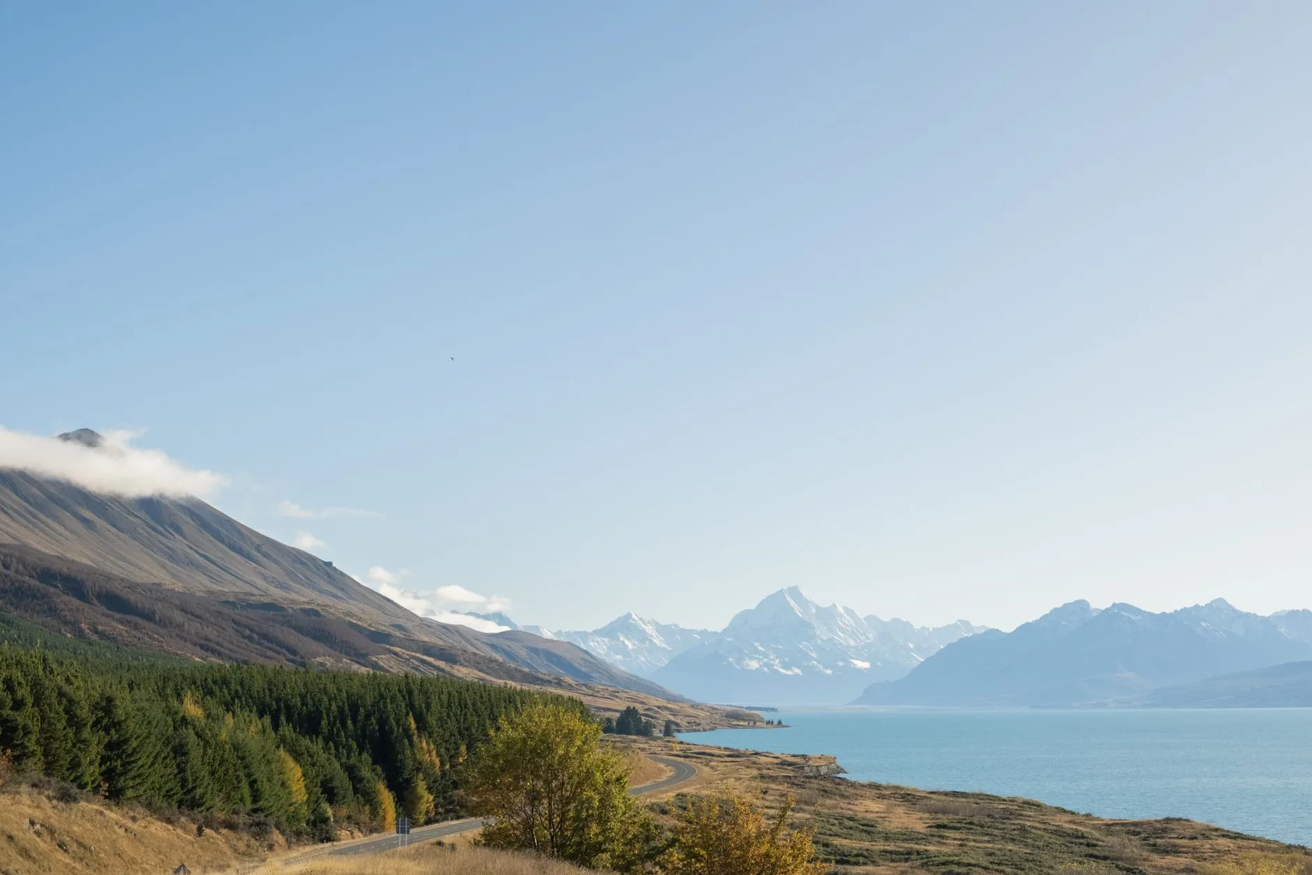 Route longeant un lac face à des montagnes enneigées en Nouvelle-Zélande